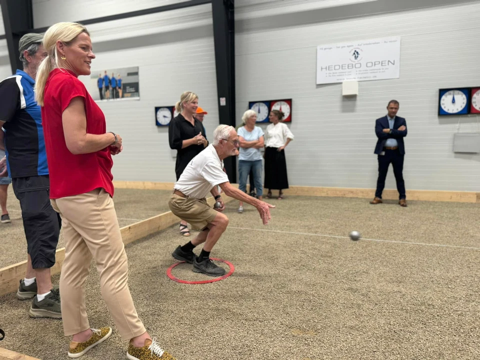 Ældreminister Mette Kierkgaard ser til mens en ældre borger kaster en petanquekugle.